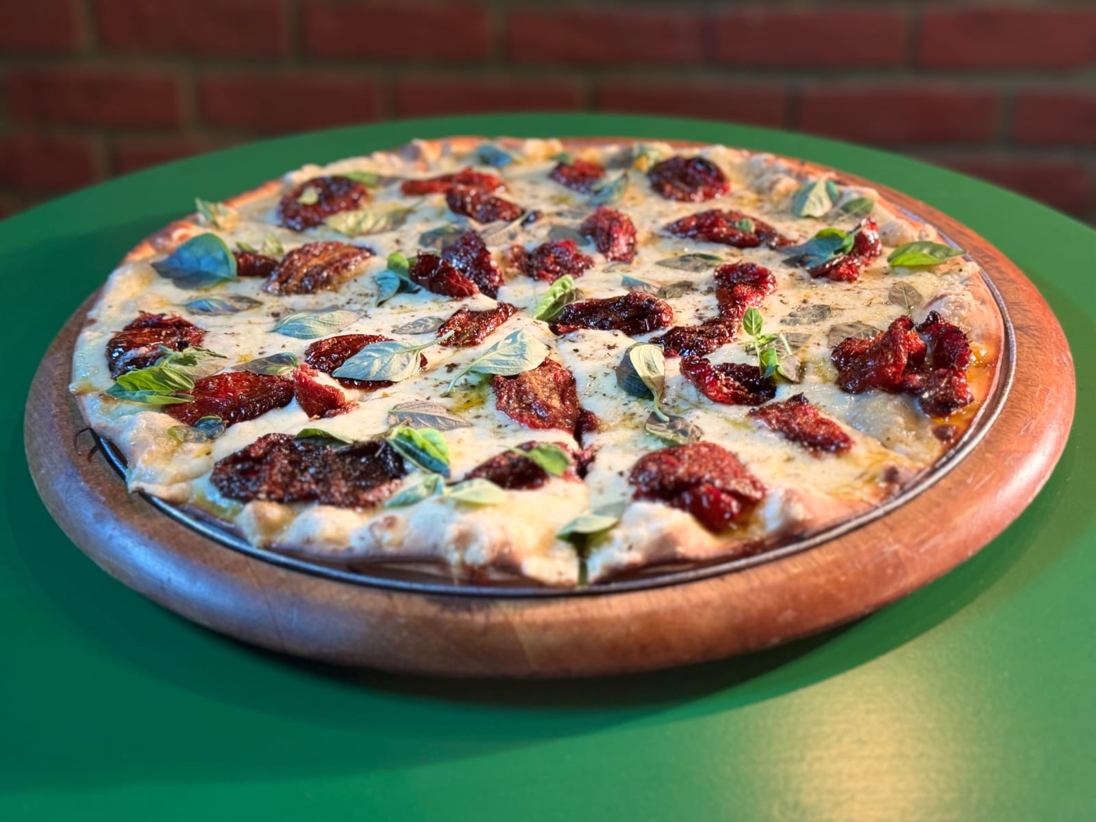 Pizza da Di Pietro com tomate seco e manjericão, servida na tábua