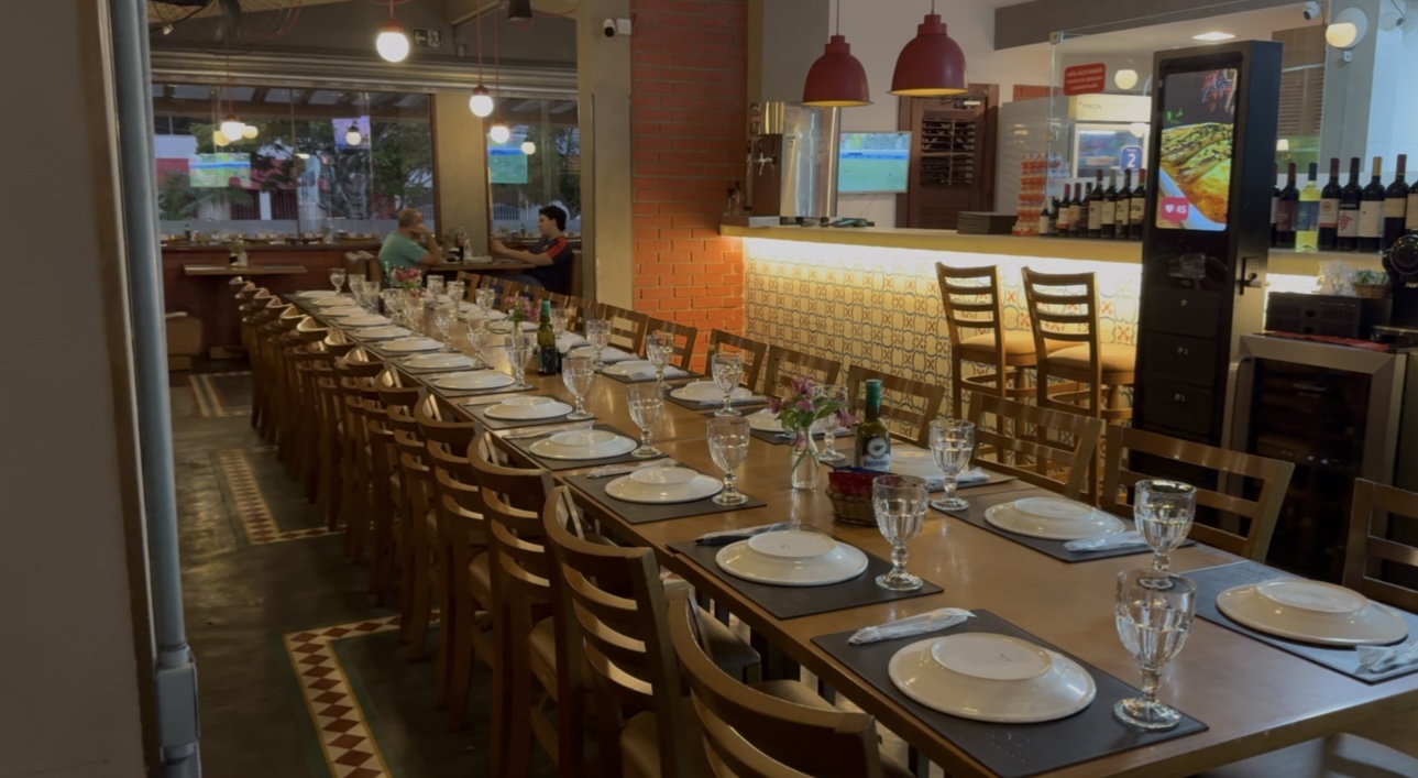 Salão principal da Di Pietro, com mesa comunitária e bar ao fundo